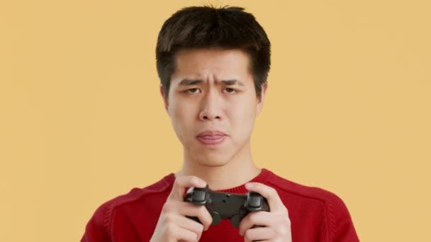 asiático chico jugando y perder vídeo juego posando sobre amarillo fondo - Metraje, vídeo