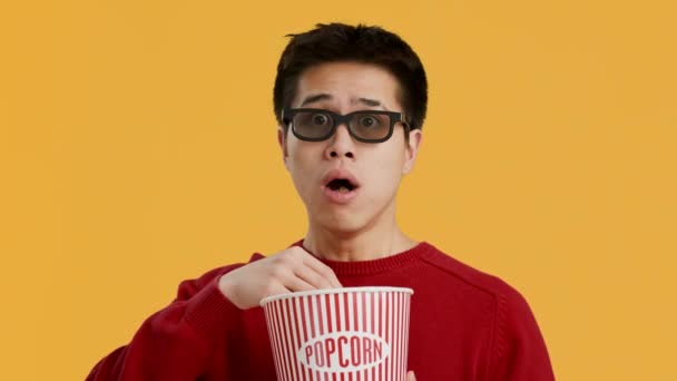 Järkyttynyt kiinalainen mies yllään 3D lasit syöminen Popcorn, keltainen tausta - Materiaali, video