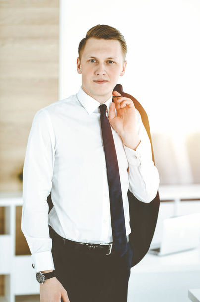 Cheerful businessman standing and looking at camera in sunny office. Headshot of young entrepreneur - Photo, image