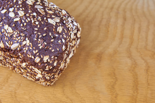 Dark rye bread with whole sunflower seeds, flaxseeds and oatmeal on top on a wooden background, copy space. - Foto, imagen