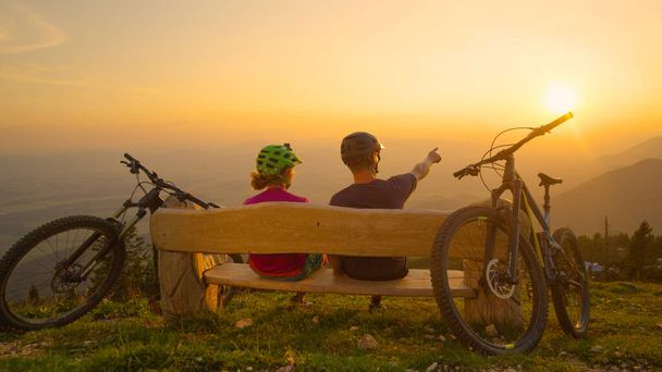LENS FLARE: Jóvenes socios ciclistas disfrutando de las vistas del paisaje iluminado de oro. - Foto, Imagen