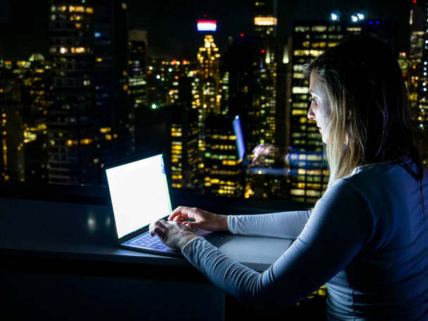FERMER : La femme est assise dans sa chambre d'hôtel au-dessus de Times Square et travaille sur un ordinateur portable - Photo, image