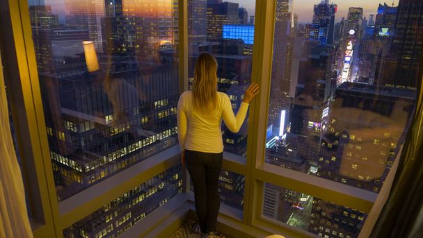 CHIUDI: La viaggiatrice sta vicino alla finestra e osserva Times Square all'alba - Foto, immagini