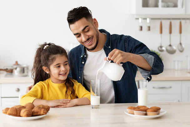 Portret szczęśliwego bliskowschodniego taty i małej córki jedzącej przekąski w kuchni - Zdjęcie, obraz