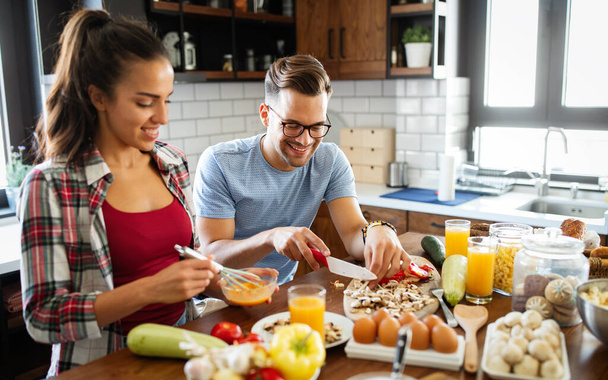 Happy young couple having fun in modern kitchen while preparing fresh food - Photo, image