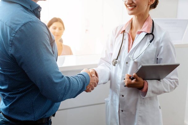 Doctor and patient shaking hands at front desk of doctors office - Фото, изображение