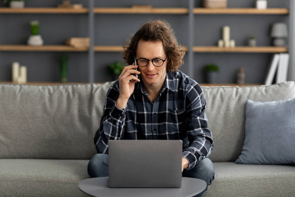 Młody człowiek rozmawiający przez telefon przy użyciu laptopa Praca online w pomieszczeniach - Zdjęcie, obraz