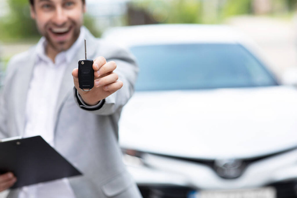 Geschäftsmann im Anzug zeigt oder gibt Autoschlüssel für Kunden, die neues Auto bekommen - Foto, Bild
