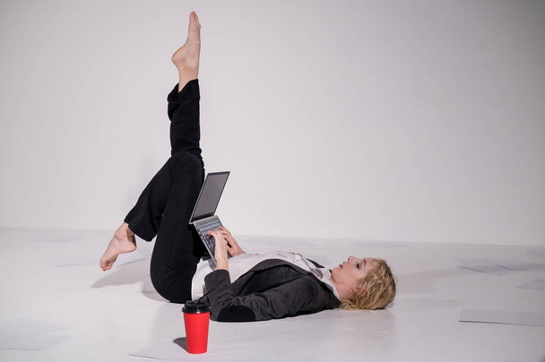 Barefoot ballerina dressed in a business suit poses for a laptop and drinks coffee. Flexible woman works at the computer - Fotoğraf, Görsel