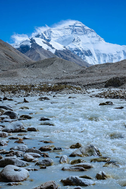 VERTIKAL: Schmutziger Bach fließt über die felsigen Ausläufer des schneebedeckten Mount Everest. - Foto, Bild