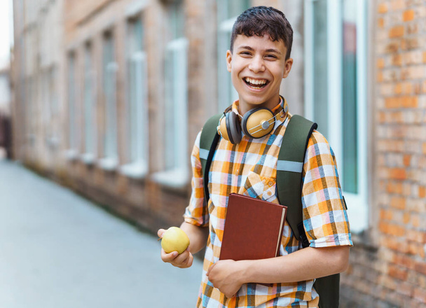 学校に行く途中の幸せな10代の男の子の肖像画、彼はアップルを食べている、教育と学校の概念に戻る - 写真・画像