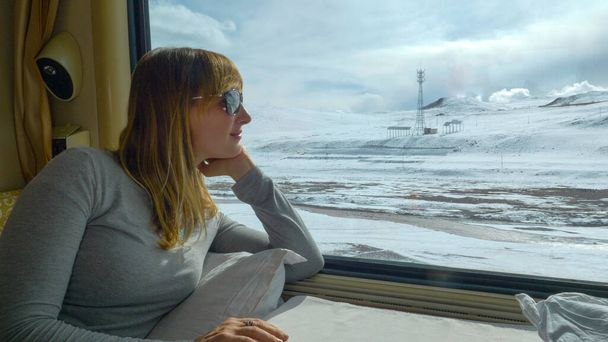 ZAMKNIJ SIĘ: Młoda kobieta obserwuje malownicze śnieżne Himalaje podczas jazdy pociągiem. - Zdjęcie, obraz