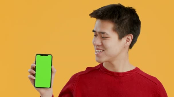 Aziatisch Guy toont telefoon met groen scherm op gele achtergrond - Video