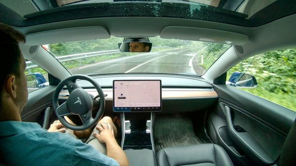 CLOSE UP: Young Caucasian man lets the autonomous car drive him down wet road. - Foto, immagini