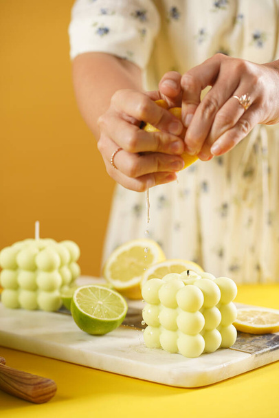 Female hands pressing lemon juice on a bright green bubble candle surrounded by lemon and lime halves, fresh thyme - Foto, Imagen