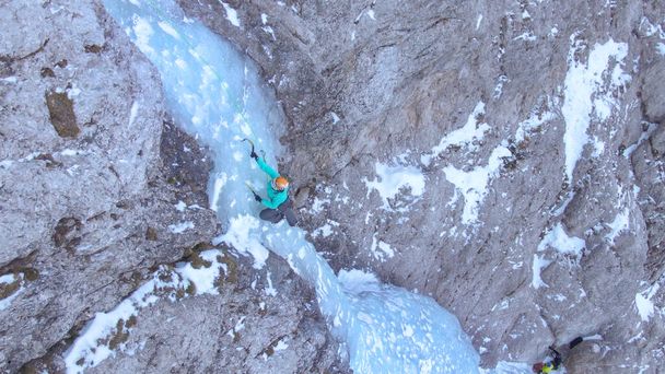 DRONE: Alpinista feminina colocando seus picaretas de gelo enquanto subia uma cachoeira gelada. - Foto, Imagem
