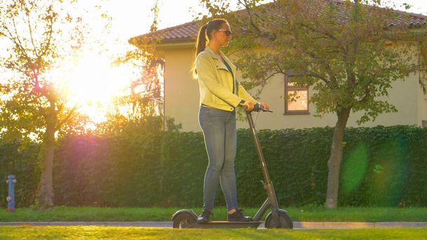 SUN FLARE: Millennial Girl fährt mit einem Hightech-E-Scooter durch die Vorstädte. - Foto, Bild