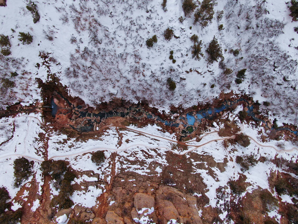 TOP DOWN Lecący wysoko nad turkusowym strumieniem kaskadowym przez śnieżną pustynię - Zdjęcie, obraz