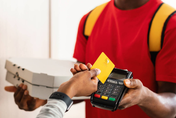 Cliente irreconocible que paga el mensajero que pone la tarjeta de crédito a la terminal en interiores - Foto, imagen