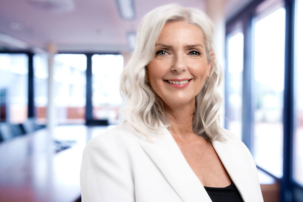 Portrait of grey haired businesswoman looking at camera and smiling while standing in the meeting room. Copy space.  - Foto, immagini