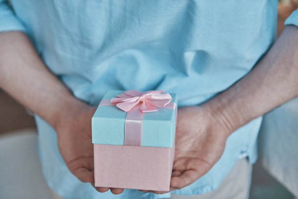 Close-up of man holding gift box behind his back - Foto, afbeelding