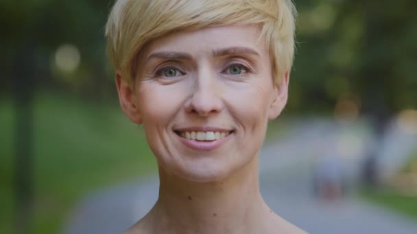 Female portrait outdoors middle-aged caucasian woman mature lady blonde short haired businesswoman standing outdoor looking at camera smiling sincerely happy smile face with wrinkles natural make-up - Footage, Video