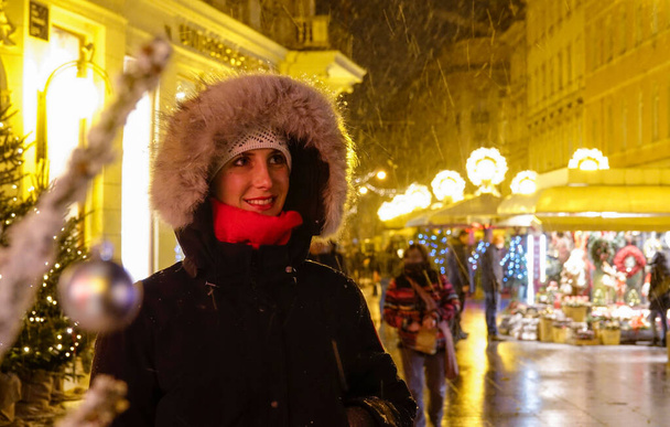 Gülümseyen kız kar yağışlı bir kış gecesinde piyasaya bakıyor.. - Fotoğraf, Görsel