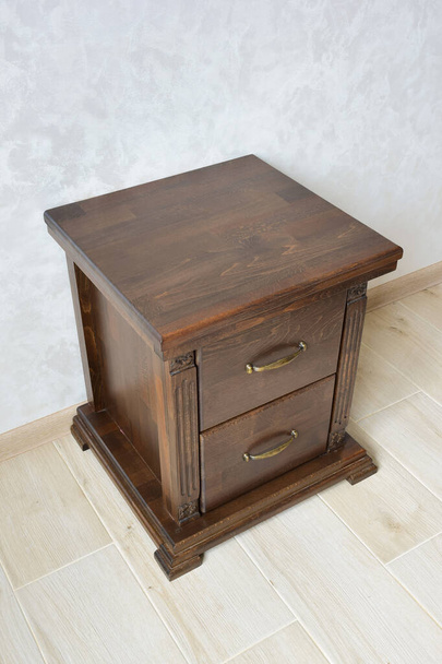 Decorative brown wooden bedside table with two drawers near the wall on a tiled floor. For bedside accessories - Photo, Image