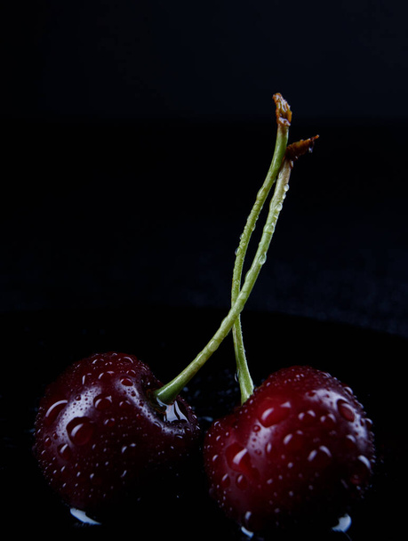 Две спелые ягоды вишни с капельками воды на кожуре на черном фоне. - Фото, изображение