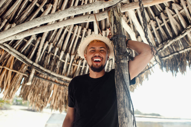 Jovem turista sorrindo enquanto estava de pé sob guarda-chuva de bambu na praia - Foto, Imagem