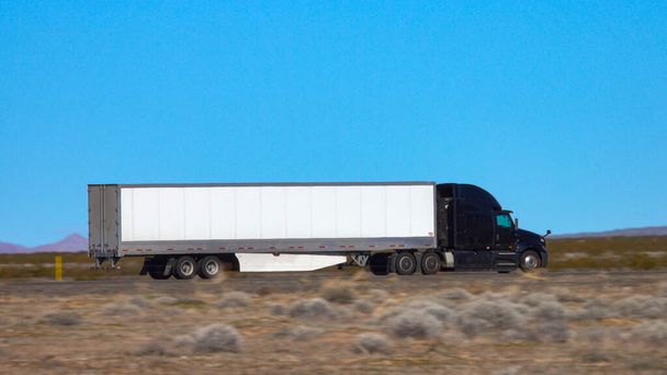 閉鎖:砂漠を横断する州間高速道路沿いの黒いトラックの速度 - 写真・画像