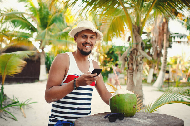 Fiatal turista mosolyog, miközben ellenőrzi okostelefon nyaralás közben a szigeten - Fotó, kép