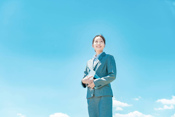 Joven mujer de negocios asiática de pie contra el cielo azul - Foto, imagen