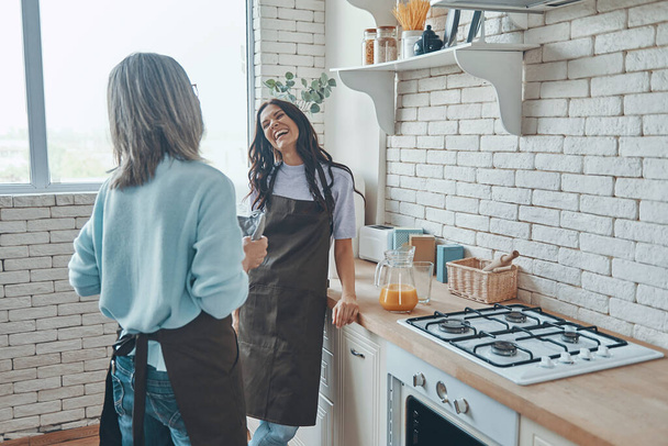 Beautiful young woman and her mother communicating while spending time at the domestic kitchen - 写真・画像