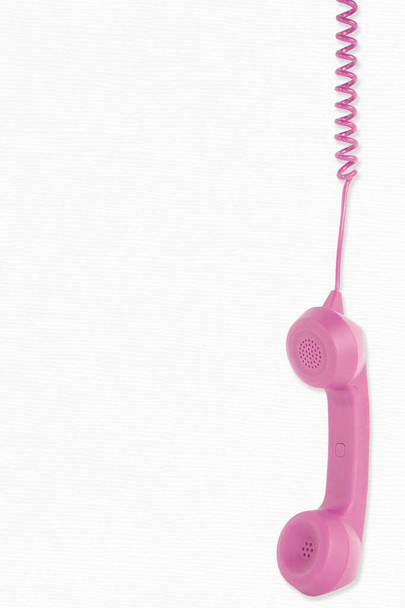 retro pink telephone receiver dangling from telephone cord on white background - Photo, Image