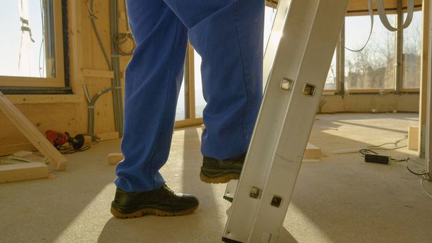 CERRAR: Primer plano de las piernas del trabajador mientras sube por una escalera de aluminio. - Foto, Imagen