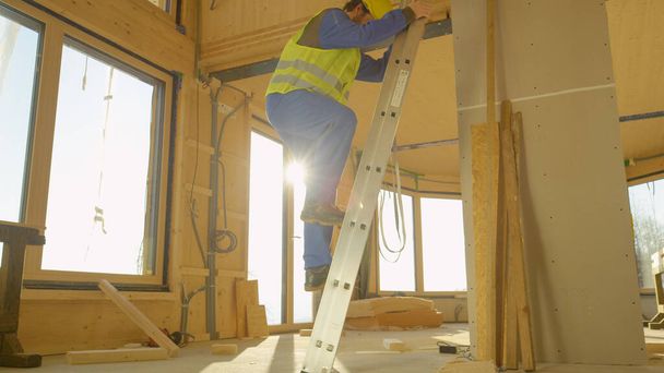 CLOSE UP: Builder climbs down from stepladder placed inside prefabricated house - 写真・画像