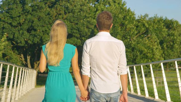 CLOSE UP Unerkennbarer Mann und verliebte Frau halten sich beim Überqueren einer Brücke an Händen - Foto, Bild