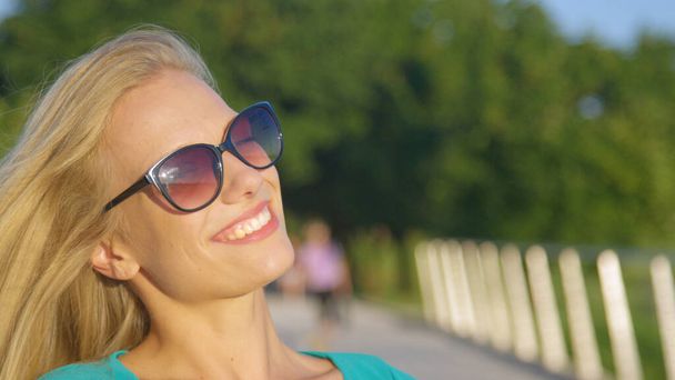 ZAMKNIJ SIĘ: atrakcyjna blondynka uśmiecha się do kamery w zielonym parku. - Zdjęcie, obraz