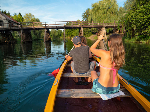 FECHAR-SE: Ativos turistas masculinos e femininos remar uma canoa sob uma ponte de madeira. - Foto, Imagem