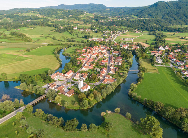 AERIAL: Repül felett egy gyönyörű kis falu épült egy kanyargó folyó körül. - Fotó, kép