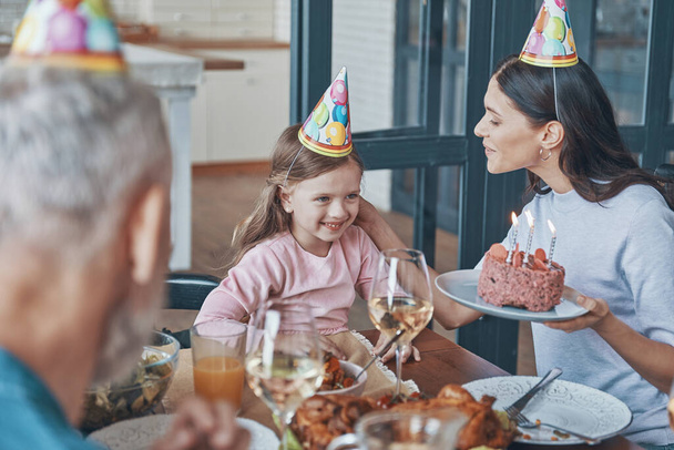 Happy family celebrating birthday of little girl while sitting at the dining table at home - Photo, Image
