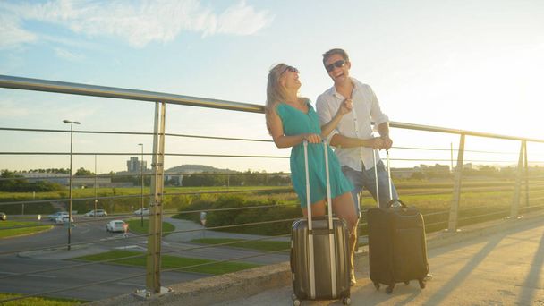 LENS FLARE: Casal alegre ri enquanto espera pelo traslado do aeroporto ao pôr do sol. - Foto, Imagem
