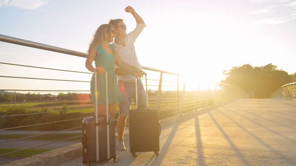 LENS FLARE Západ slunce svítí na radostný pár čekající s zavazadly jít na dovolenou - Fotografie, Obrázek
