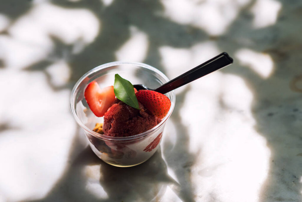 Frisches rotes Erdbeer-Sherbate-Joghurt-Eis im Plastikbecher auf dem Tisch mit hellem Schatten. Gesundes Essen von süßer Wüste. Fettarme Kalorien. - Foto, Bild