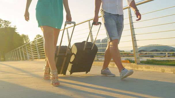 LENTE FLARE: Donna in tacchi alti e fidanzato trascinare valigie per l'aeroporto. - Foto, immagini