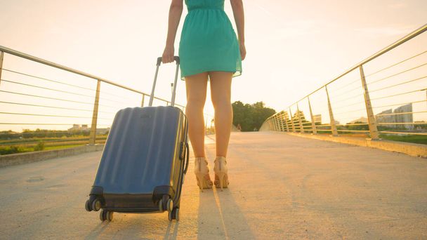 Nízký úhel: Mladá žena stojí se svými zavazadly ve zlatém večerním slunci. - Fotografie, Obrázek