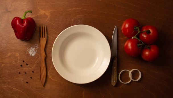 Tyhjä levy ja tomaatteja paprikalla ja sipulilla ruskealla taustalla - Valokuva, kuva