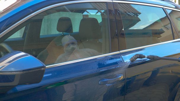 Nicht wiederzuerkennender Virologe besprüht Türgriff von Auto mit antiviralem Spray - Foto, Bild