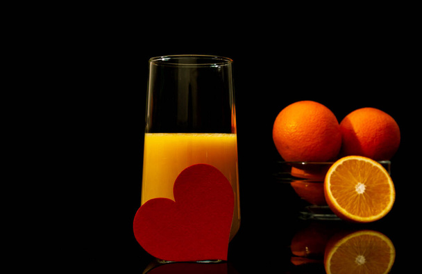 Jus d'orange dans un verre avec des tranches de fruits planant sur le fond noir foncé - Photo, image